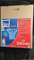Box showing front display of the Spalding Championship Series basketball rim and net, featuring NBA graphics and product details.