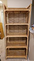 Full view of the vintage rattan wicker shelf showing its tall upright structure with five shelves and woven rattan lattice back.
