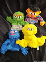 Four Sesame Street hand puppets arranged on a black background: Big Bird, Oscar the Grouch, Ernie, and Grover.