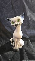 Front view of vintage Japanese ceramic Siamese cat figurine showing detailed facial features, green eyes, and black accents on ears and paws.