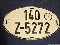 Full view of oval German export license plate with black raised numbers and letters and circular validation area.