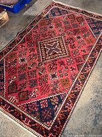 Angled view of entire rug displaying red field and navy geometric corners
