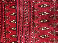 Close-up of the rug showing detailed geometric pattern and border design in red, brown, black, and cream.