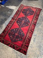 Full view of the Zanjan runner rug laid flat on concrete floor showing the overall design, red field with three blue geometric medallions and patterned border.
