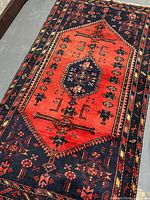 Angled top view showing full rug with red central medallion and navy border with geometric motifs.