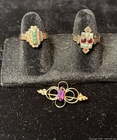 Frontal view of two rings and brooch displayed on black holder