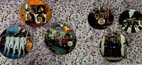 Photo showing all 6 Beatles commemorative plates arranged on floral background, each plate featuring different Beatles artwork and imagery.