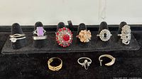 Front view of all rings displayed on black velvet tray, showing mix of rhinestone, sterling, and metal bands.