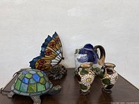Photo of butterfly and turtle stained glass lamps, porcelain fish pitcher, and two Italian vases on table