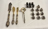 Full lot showing antique German Stahl cutting utensils, sterling silver ladle, salt and pepper shakers, and metal name holders all laid out on white surface.