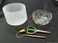 Photo showing frosted glass pot, cut glass bowl, brass candle snuffer, and green herb scissors on black background