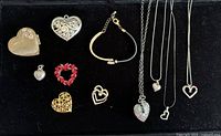 Top view image displaying all 11 heart-themed jewelry items laid out on black background, including pendants, brooches, a locket, and a bracelet.