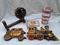 Lot showing wooden spinning wheel souvenir, framed fruit label picture, glass Art Deco vase, and two wooden wall plaques of train and stagecoach.