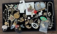 Top view of a tray of mixed costume jewelry with various styles and pieces including necklaces, brooches, earrings, and pins.