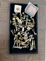 Tray with a mixed assortment of cufflinks and tie clips in gold and silver tones, including some mounted on cards and small clear bags.