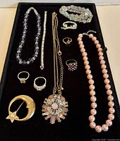 Full top view of the jewelry lot showing necklace, bracelets, rings, and brooches arranged in a black tray.
