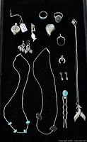Full lot showing various silver-tone jewelry including rings, necklaces, earrings, pendants and hair accessories arranged on black background.