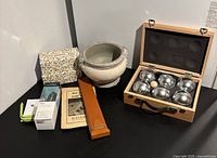 Wide angle photo showing all items in the lot: petanque set in wooden box, two boxes of Baby Bomba socks, vintage slide rule with booklet, Fitbit Flex 2 with box and accessories, pottery flower pot.