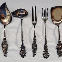 Full view of 5 of the utensils showing various types including spoons and forks with floral handle designs, tarnished silver-tone metal.