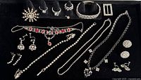 Assorted clear and red stone rhinestone jewelry displayed on black velvet including brooch, necklaces, bracelets, earrings, and rings.