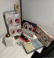 Mixed lot photo showing boxed iBasket frosted glass plates, wooden peg rack, crystal relish dish, vintage nutcracker, steak knives, ceramic jar, and Sephora perfume box.