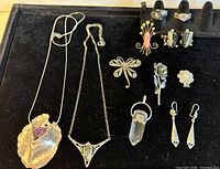 Photo showing 11 sterling silver jewelry pieces arranged on black velvet display including necklaces, rings, earrings, and brooches.