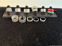 Front view of 11 sterling silver rings with varied textured and patterned designs including a red and green layered ring.