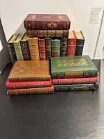 Photo showing the front and spine view of 22 books of varying colors and gold embossing, stacked and standing.