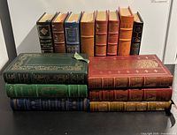 Photo of all 22 hardcover leather-bound volumes arranged on a table, showing variety of colors and gold detailing, including two slipcases with gold designs and a bookmark.