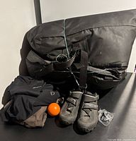 Black foldable Thule car top box resting on surface with sports gear around it including bike shoes, bike shorts, orange squish ball, and Nike tee.
