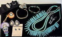 Lot of Native American-themed turquoise and sterling silver jewelry displayed in black tray including necklaces, rings, earrings, bracelets, and pins.