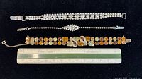 Top view of three vintage bracelets laid on a white background with a ruler showing their length.