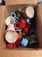 Box with assorted vintage Solo cup holders in blue, red, green, white, and orange along with white plastic cup inserts, some still in original packaging.