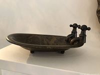 Side view of the oval antique brass soap dish showing the patina and two faucet-like taps.