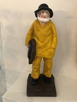 Front view of antique cast iron fisherman doorstop painted yellow and black, showing facial details and held object.