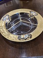 Top view of the round serving bowl showing the three internal compartments and enameled floral decoration on the gold-tone rim.