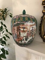 Front view of the jar showing detailed painting of figures and floral designs, rounded shape and lid with finial.