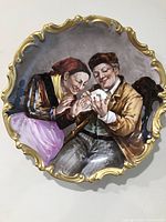 Full view of antique Limoges porcelain wall plate featuring hand painted scene of two elderly figures and gilded ornate border.