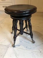 Front angled view of antique wooden piano stool showing round seat, turned legs, and claw feet with glass balls.