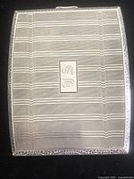 Front view of rectangular sterling silver cigarette case showing intricate engraved border, horizontal and vertical line pattern with center monogram initials.