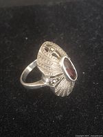 Side angled photo showing oval garnet or pink ruby gemstone set in detailed sterling silver ring with marcasite accents.