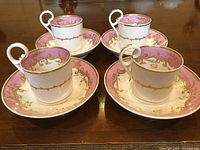 Four antique coffee cups with matching saucers arranged on wooden table, showing front and handle details