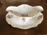 Front view of Herend two-handle gravy boat with floral pink and green decoration and gold trim on edges and handles.