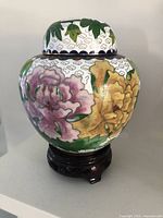 Front side showing floral designs in pink and yellow, on white background with golden outlining, wooden stand visible.