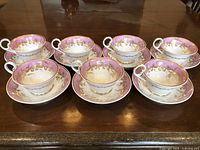 Seven porcelain tea cups with matching saucers arranged on a wooden table, showing the full set.