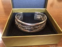 Front view of sterling silver cuff bracelet in display box showing woven design and polished edges.