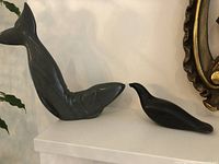 Two Inuit soapstone sculptures displayed on a white surface, a whale and a bird sculpture side by side.