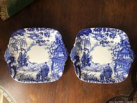 Two Royal Crown Derby Blue Mikado square handled cake plates side by side on wooden surface.