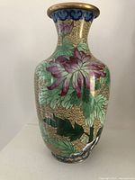 Front view of mustard colored cloisonne vase with pink flowers and green leaves, brass rim, showing detailed enamel and wire work.