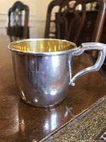 Side view of the sterling silver baby cup showing engraved initials and handle design on polished exterior.